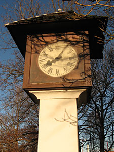Outdoor clock in front of trees, by factory entrance, time: 8:05